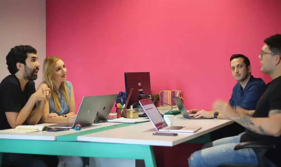 Cuatro personas del equipo de Koombea conversando entre dos escritorios, con portátiles abiertos