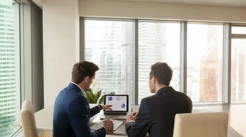Two businessmen staring at a computer in a conference room.